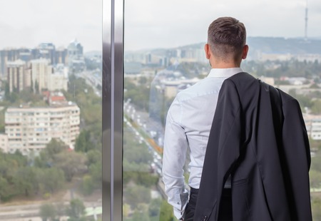 Young businessman at office on the top floor at the front of the window to standing back. with panoramic views of the cityの写真素材