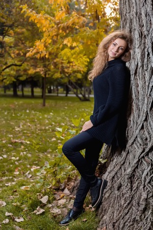 Beautiful woman in black sweater, posing in autumn Park near the treeの写真素材