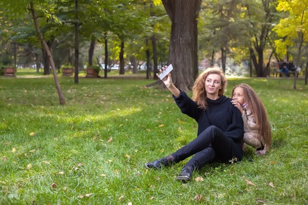 Mother with daughter seven years old in autumn Park at sunset. A woman makes a selfie together with his childの写真素材