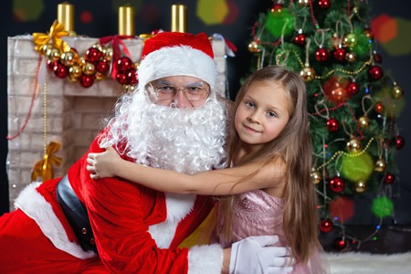 Santa Claus and a girl in a dress. Christmas Scenes. The child hugging Santaの写真素材