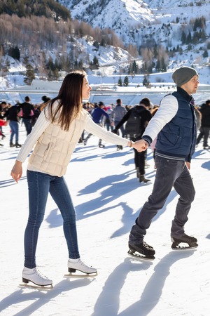 Loving couple skating together holding hands. Mountains in the backgroundの写真素材