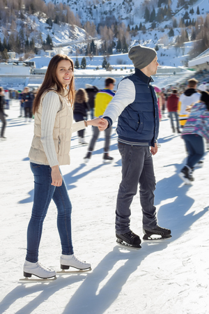 Loving couple skating together holding hands. Mountains in the backgroundの写真素材