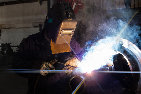 A skilled welder is making a weld on a pipe joint 