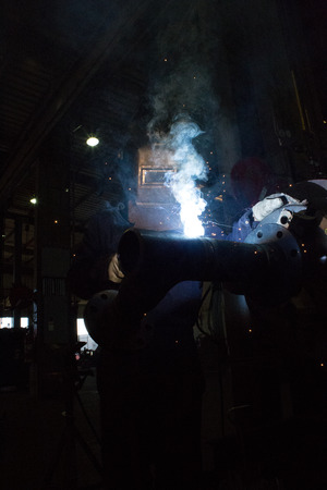 A skilled welder is making a weld on a pipe joint 