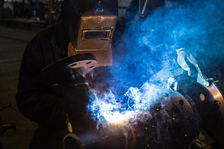 A skilled welder is making a weld on a pipe joint の写真素材