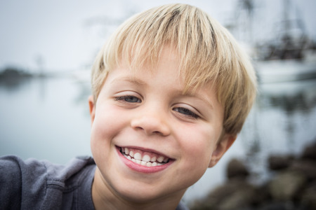 A happy little 5 year old smiling for the camera on the rocks at the harbor on an overcast day の写真素材