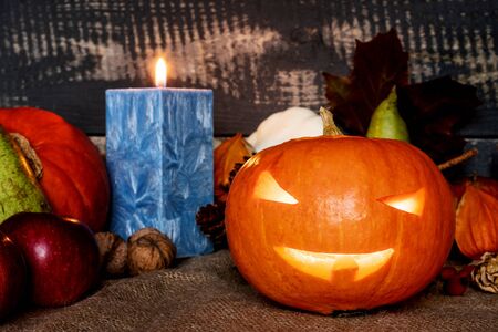 Halloween concept. Carved pumpkin with candle on jute bag surrounded by autumn fruit with background from old planks.の写真素材
