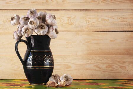 Mallets of garlic in black gold decorated vase on colored tablecloth with wooden background. Copy space.の写真素材