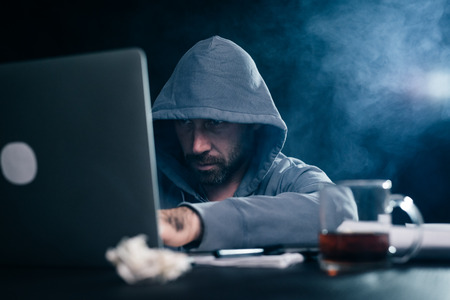 A computer hacker is typing on a laptop in a smoky room. Dark backgroundの写真素材