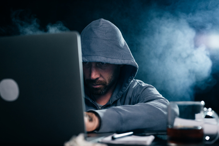 A computer hacker is typing on a laptop in a smoky room. Dark backgroundの写真素材