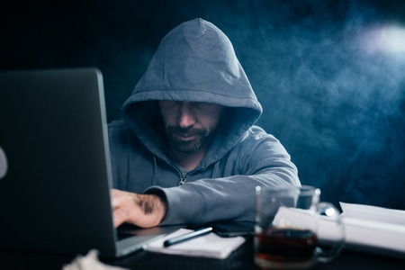 A computer hacker is typing on a laptop in a smoky room. Dark backgroundの写真素材