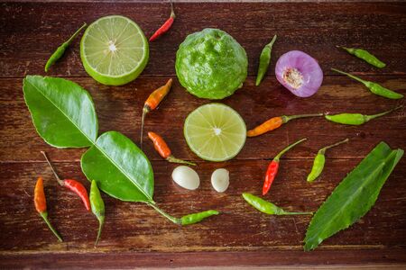 A mixture of spicy Thai food "Tom Yum", spicy soup with lemon, chili, onion, bergamot, lemon, kaffir lime leaves, top view, put on woodの写真素材
