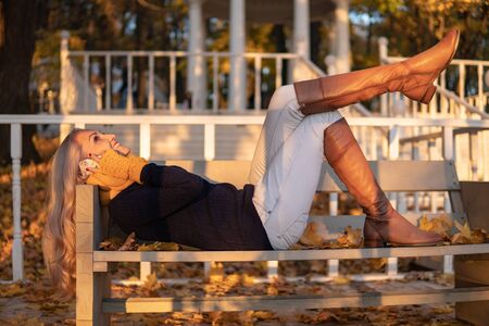 Autumn girl talking on the phone while lying on a bench in a park, after a walkの写真素材