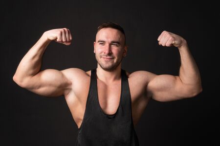 Young man showing biceps over black background