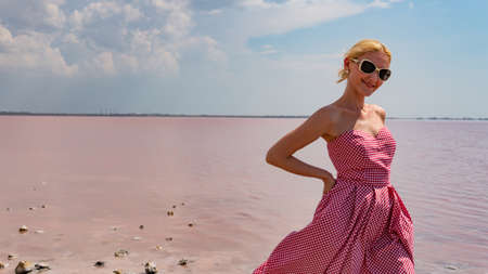 Girl on the background of a pink lake, salty seas, in a red dress in sunglassesの写真素材