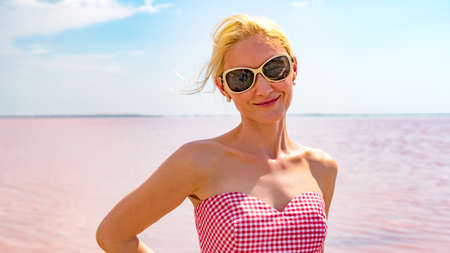 Smiling woman in a beautiful dress with a lovely smile on the background of a pink lake during the day and summerの写真素材