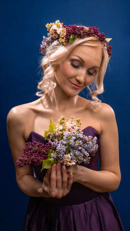 Blessed young beautiful in a lilac wreath with beautiful eyes blooms on a blue background, happy dayの写真素材