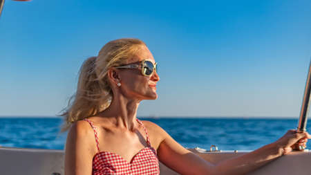 Smiling sits on a yacht, a young woman smiles at the camera on the horizon sea, monochrome glasses,...