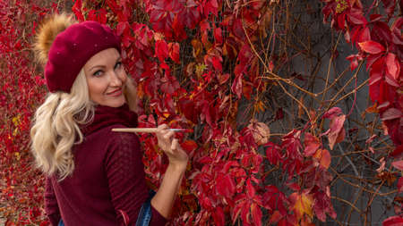 Beautiful girl artist stands near the wall of leaves with a brush in a beretの写真素材