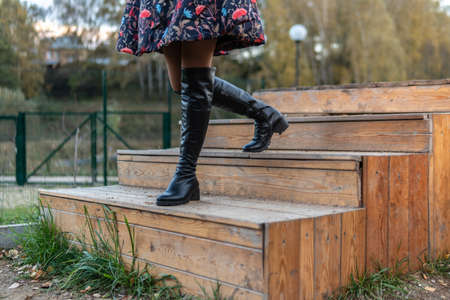 A beautiful girl walks up the stairs and in a burgundy palette and biret, smiles at the camera in black clothes, in the fall against the background of trees, blue clouds.の写真素材