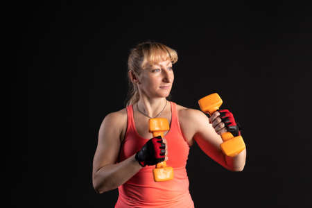Fitness woman on a step platform with a barbell with dumbbells. Going in for sports on a black...