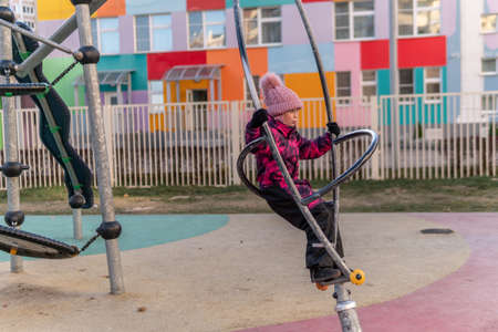 Playground a girl plays on a spinning pipe, in the entertainment center she is wearing a warm jacket and a hat, she is cheerful.の写真素材