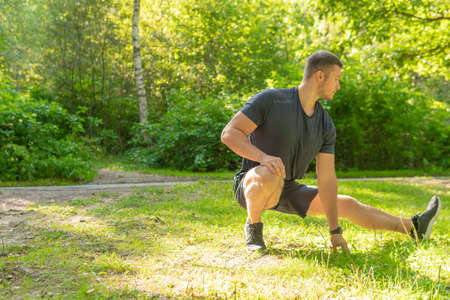 A young enduring athletic athlete is doing stretching in the forest outdoors, around the forest, oak trees.healthy forest, fitness young wellness marathon, wellbeing. running, runners stretchesの写真素材