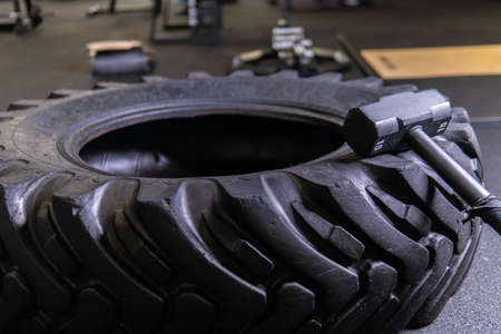 A tire on a black background with a sledgehammer lies for crosfit fitness wheel sledgehammer workout body sport, for fit power in lifestyle healthy tyre, active club. Equipment indoors cross,の写真素材