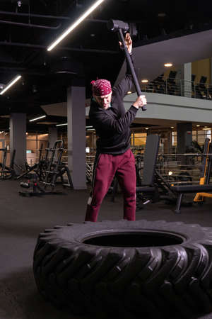 A man hits a sledgehammer wheel in fitness, the concept of a healthy lifestyle male sledgehammer active hit sport, for strength exercise for adult for bodybuilder wheel, strike ethnic. Club energy ethnity, strenghtの写真素材