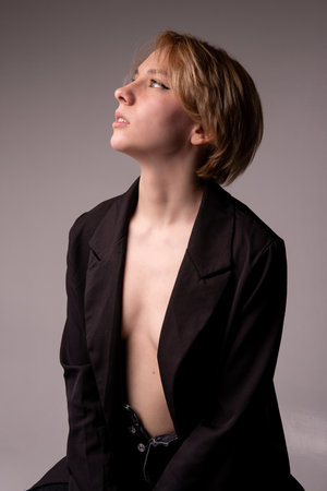 A girl sits looking up in a blonde suit with open breasts Adult attractive background bare black, from caucasian female for fresh and healthy model, portrait seductive. Sexy studio swimsuit, whiteの写真素材