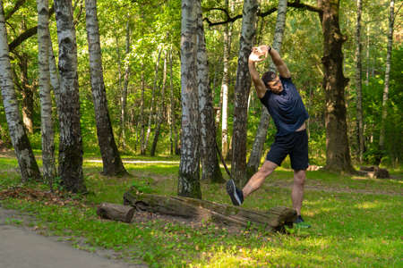 A young enduring athletic athlete is doing stretching in the forest outdoors, around the forest, oak trees.active athlete forest, fitness trail fit recreation woods Summer body running, runners stretchesの写真素材