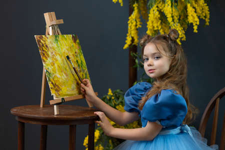 A girl sits near a mimosa and paints a picture in a blue dress mimosa brush child girl, from dress holding in beauty for smile happy, blond bloom. 8 march nature face, person pretty day pictureの写真素材