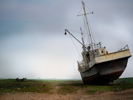 Abandoned fishing ship on the shore against the background of morning fog