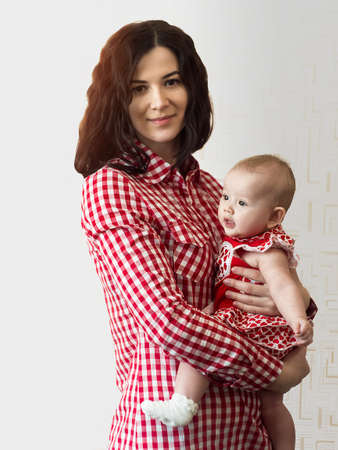 The photo shows a young mother with a baby in her arms on a white background. Bright photo with smiling people in the same clothes.の写真素材