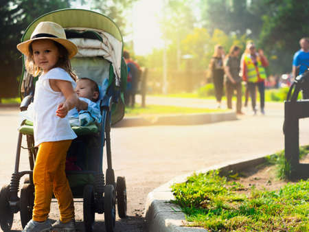Sunny summer photo of a child in a hat rolling a carriage with a babyの写真素材