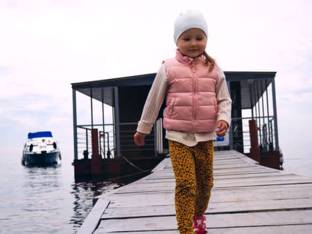 A photograph of a child walking along the pier at sunset with a calm sea in the backgroundの写真素材