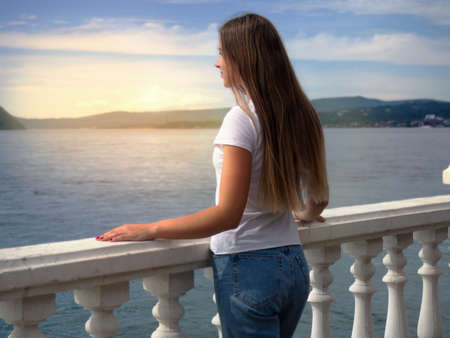 Photo of a girl looking into the distance against the backdrop of a lake, mountains and sunsetの写真素材