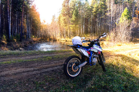 Photo of an enduro motorcycle against the backdrop of a small lake and picturesque nature on a summer dayの写真素材