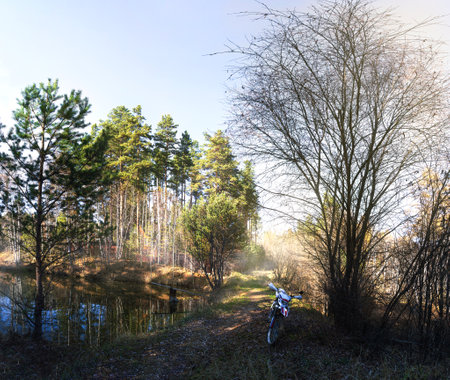 Panoramic photo of an enduro motorcycle against the backdrop of a small lake and picturesque nature on a summer dayの写真素材