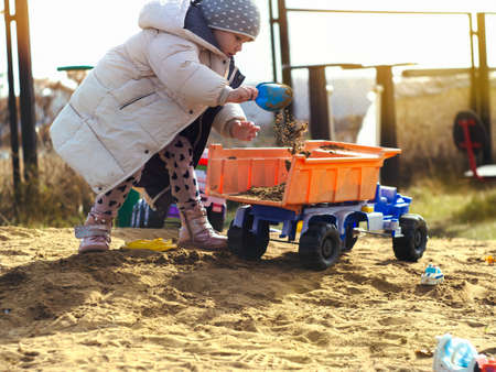 Girl picks up sand in the back of a toy truckの写真素材