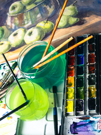 Watercolor paints, brushes and apple on a wooden table. Art concept.の写真素材