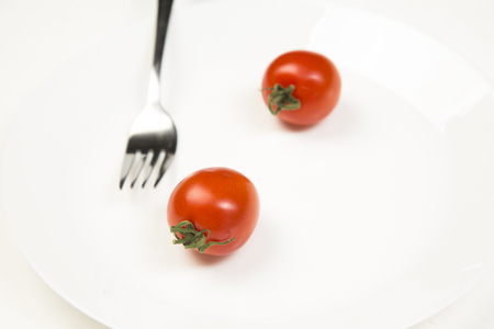 Red tomato with a fork in a white plate on a white backgroundの写真素材