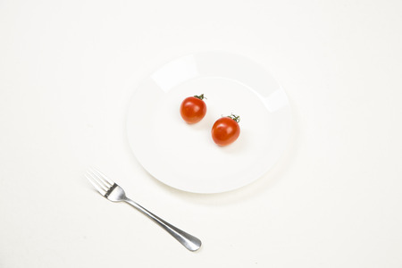 Red tomatoes on a white plate with a fork at the side on a white backgroundの写真素材