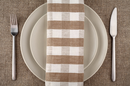 Table setting. Beige plate, fork, knife and beige linen napkin and tablecloth.