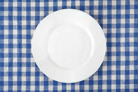 Empty white plate on checkered tablecloth.の写真素材