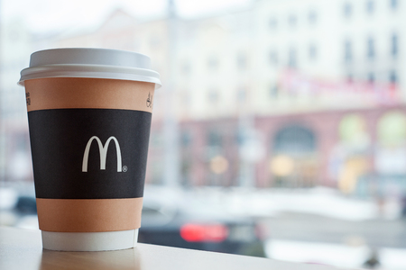 Minsk, Belarus, February 18, 2018: Paper cup of coffee with McDonald's logo on table near window on background of city in McDonald's restaurantのeditorial素材