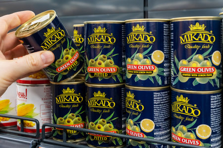 Cans of canned green olives brand mikado. A customer takes a can of green olives from a supermarket shelf. Minsk, Belarus 2022のeditorial素材