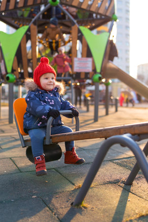 Happy beautiful little toddler girl having fun on swing in the playground. Baby smiles and laughing.の写真素材