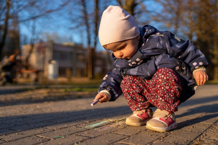 Little girl draws with chalk on the pavement in the city park.の写真素材