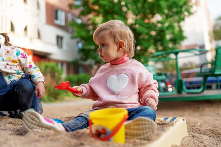 Little toddler girl sitting and playing in sandbox  on the playground near the house. Active child....
